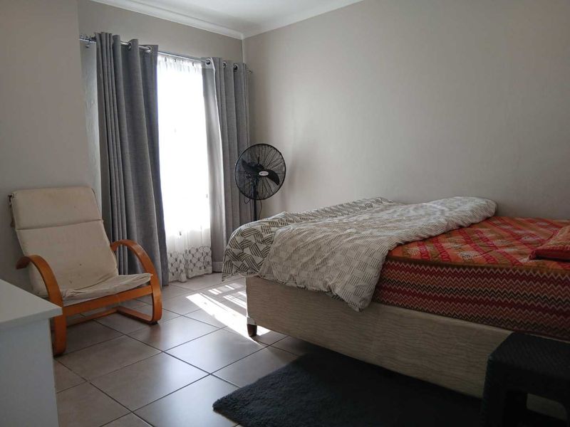 A bedroom featuring tiled flooring and large windows with curtain rails, providing natural light to the space.