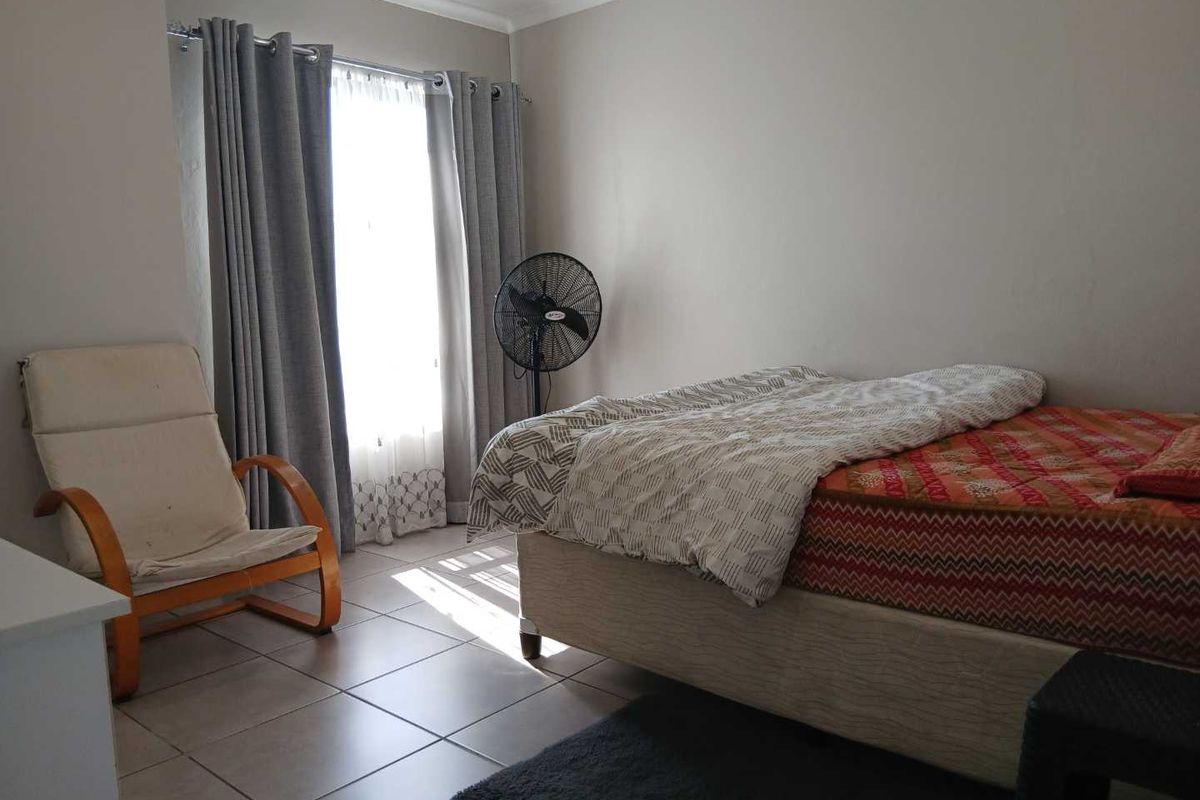 A bedroom featuring tiled flooring and large windows with curtain rails, providing natural light to the space.