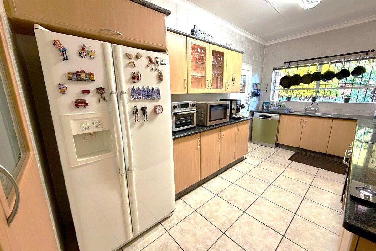 A functional kitchen featuring laminate cabinetry, granite countertops, tiled flooring, and a double sink with security bars on the window.