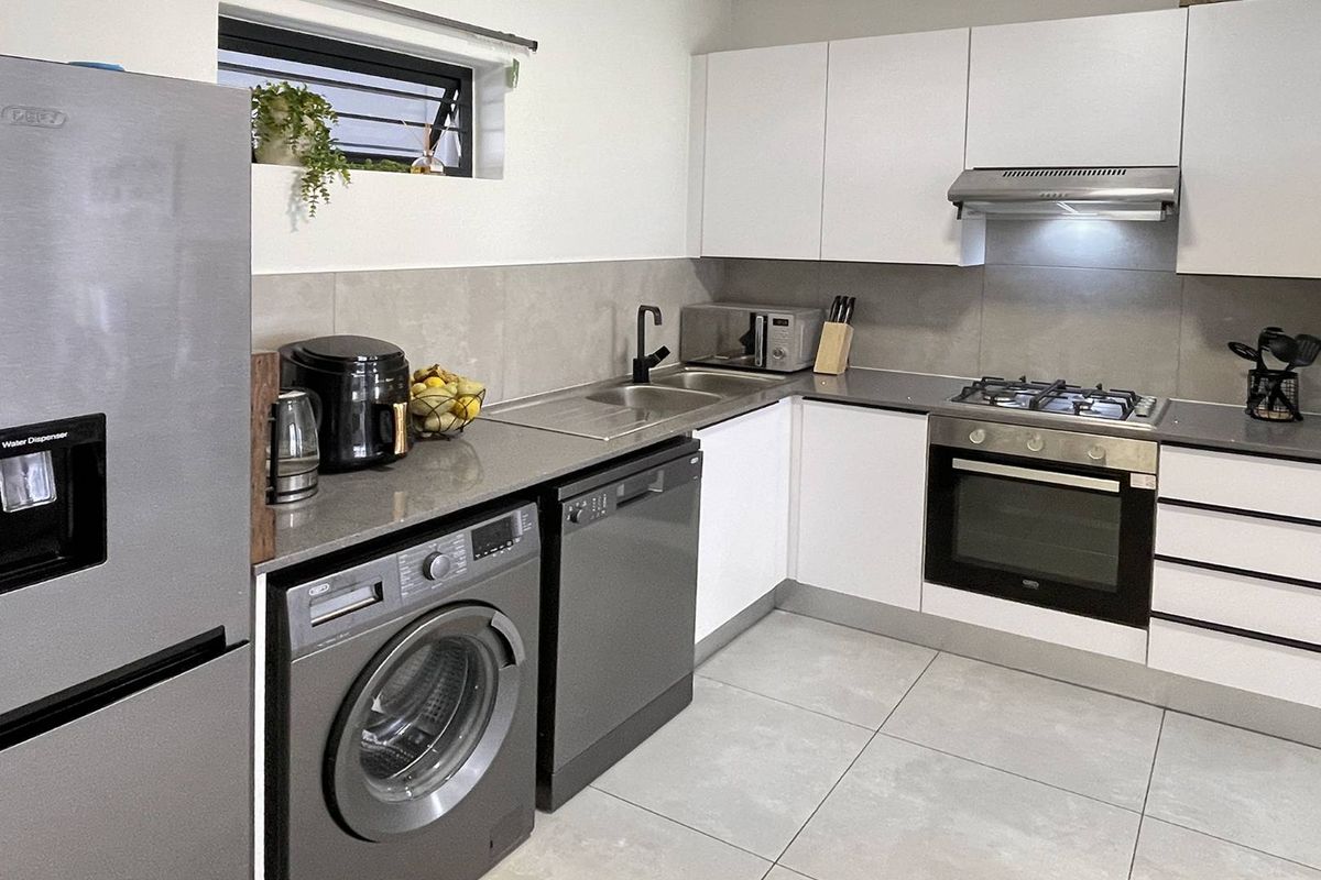 Modern kitchen featuring white cabinetry, stone countertops, integrated gas hob, oven, extractor fan, and tiled finishes with space for under-counter appliances.