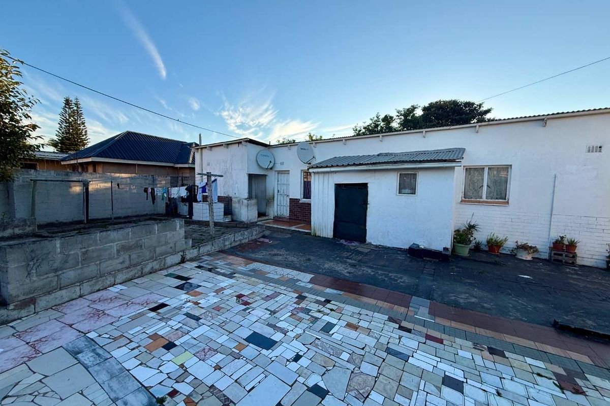 Rear exterior view of the property featuring a paved courtyard area, brick boundary wall, and basic building facade with satellite dishes.