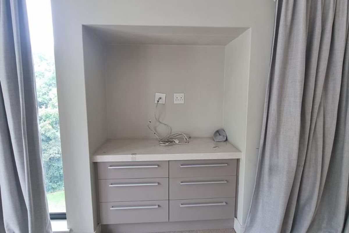 A bedroom featuring a built-in vanity or media unit with stone countertop and integrated cabinetry, flanked by floor-to-ceiling curtains.