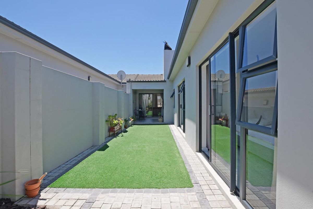 A side courtyard featuring artificial turf, paved borders, and large sliding glass doors providing seamless access to the interior living spaces.