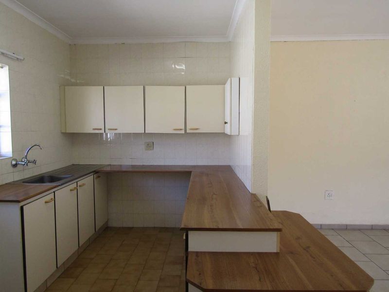 An empty, dated kitchen featuring laminate countertops, built-in cabinetry, and tiled splashbacks, offering a blank canvas for potential renovation and modernization.