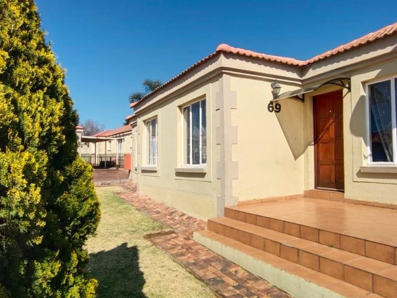 Front elevation of a townhouse featuring a tiled entrance porch, brick paved walkway, and established garden area.