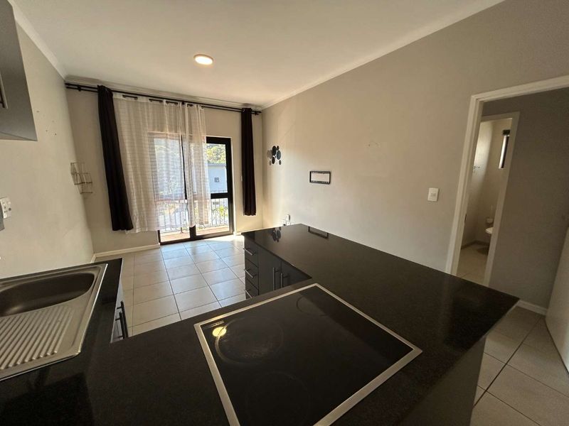 Open-plan kitchen and living area featuring granite countertops, built-in hob, tiled flooring, and direct access to a private balcony.
