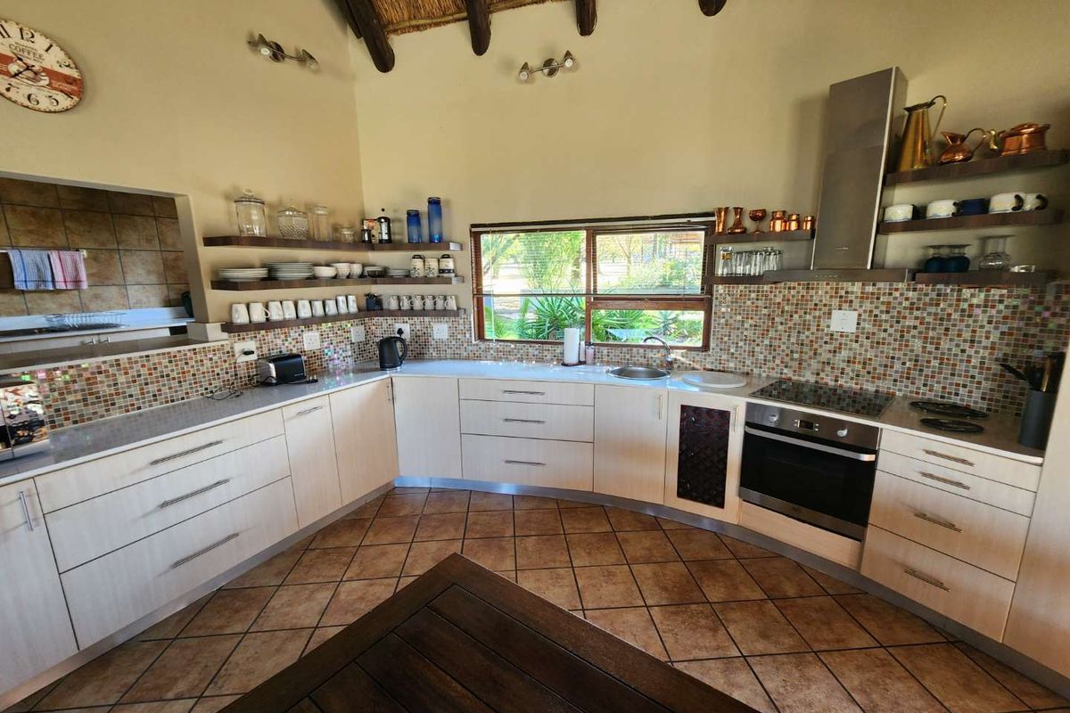 A kitchen featuring light-toned cabinetry, mosaic tile backsplash, built-in oven, extractor fan, and a vaulted thatched ceiling with exposed timber beams.