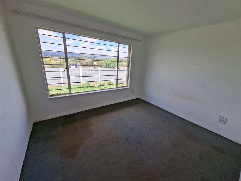 An empty bedroom featuring a large window with security bars, carpeted flooring, and neutral walls, offering a blank canvas for potential renovation.