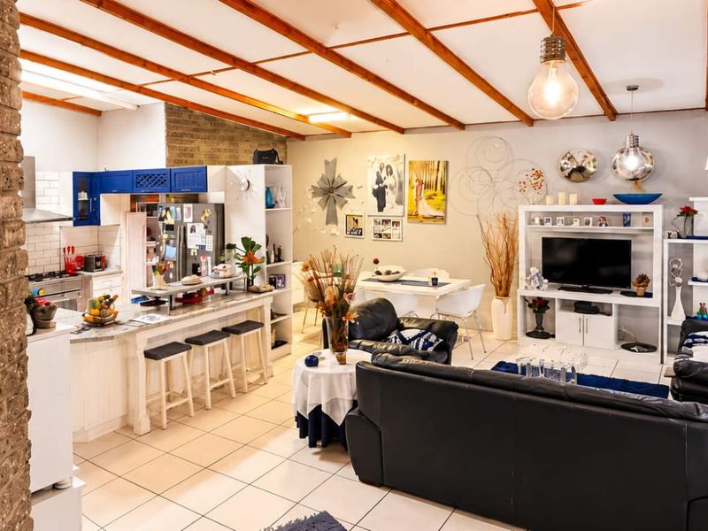 Spacious open-plan living and kitchen area featuring exposed timber ceiling beams, a brick feature wall, and tiled flooring throughout.