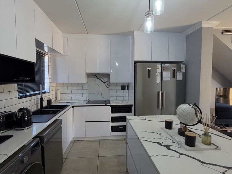Modern kitchen featuring white gloss cabinetry, marble-look quartz countertops, subway tile backsplash, and a functional island, seamlessly integrated into an open-plan living space.
