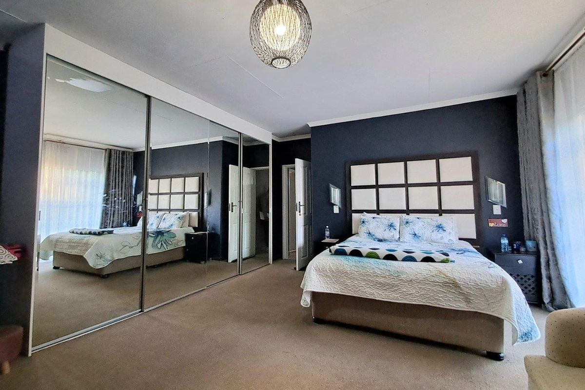 Spacious bedroom featuring large floor-to-ceiling mirrored sliding wardrobe doors, dark accent wall, and neutral carpeting.