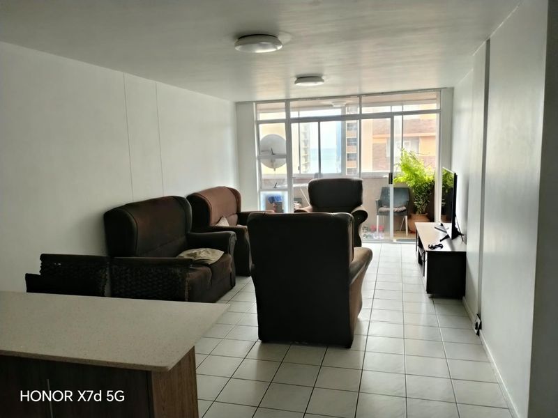 A living room area featuring tiled flooring and a large sliding glass door leading to a balcony, providing natural light to the space.