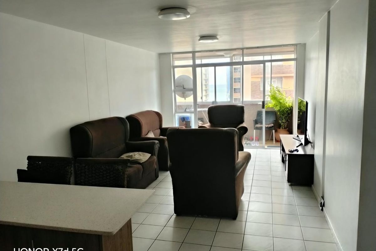 A living room area featuring tiled flooring and a large sliding glass door leading to a balcony, providing natural light to the space.