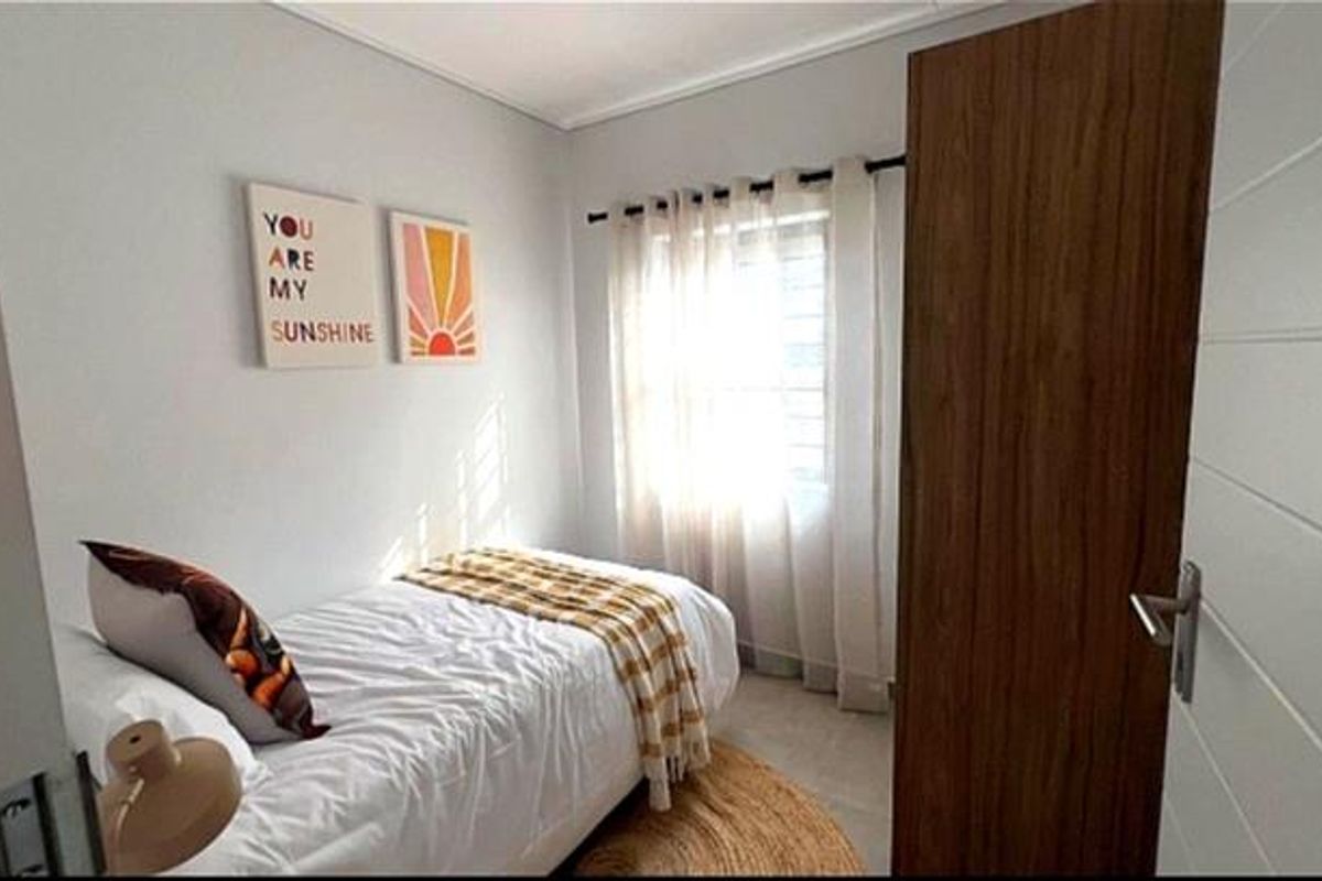 A compact bedroom featuring neutral wall finishes, a window with sheer curtains, and a modern wood-grain interior door.