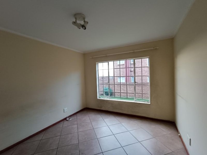 An empty bedroom featuring tiled flooring, a large window with security bars, and neutral wall finishes, ready for personalization.