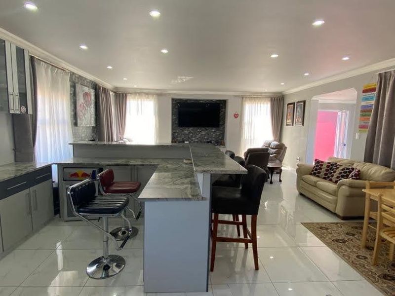 Spacious open-plan living area featuring a modern kitchen with stone countertops, breakfast bar, and sleek tiled flooring throughout the combined kitchen and lounge space.