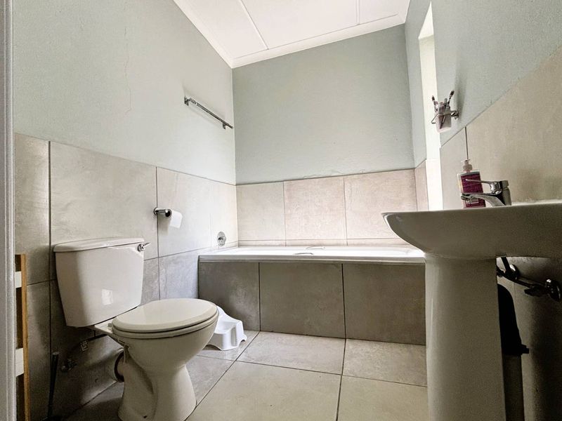 A functional bathroom featuring a pedestal basin, toilet, and a built-in bathtub with neutral wall and floor tiling.