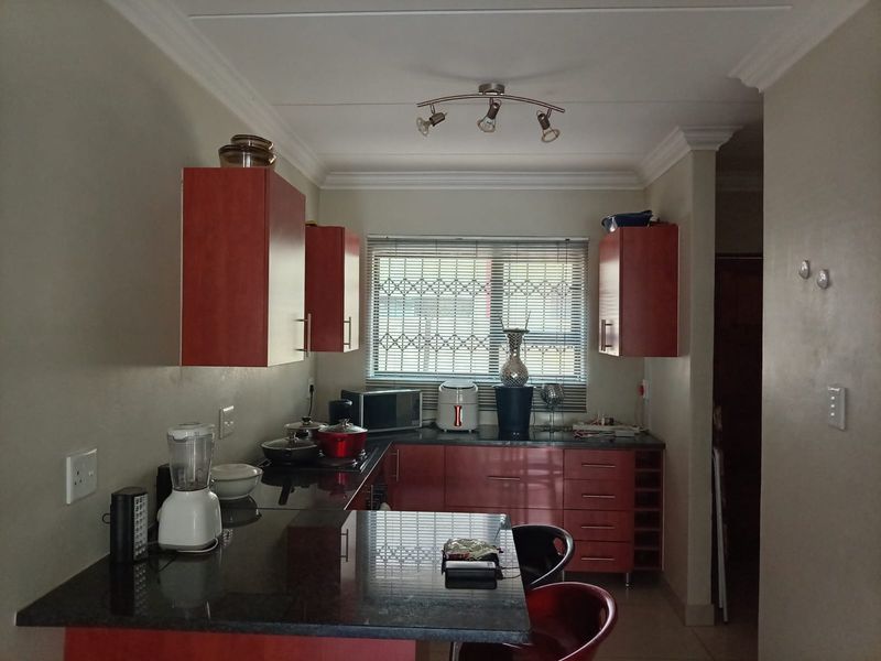 A functional kitchen featuring dark granite countertops, red cabinetry, a built-in wine rack, and security bars on the window.
