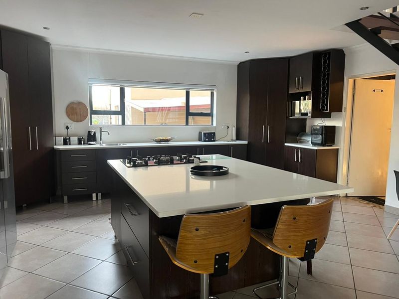 Modern kitchen featuring a large central island with a gas hob, dark wood cabinetry, stone countertops, and tiled flooring.