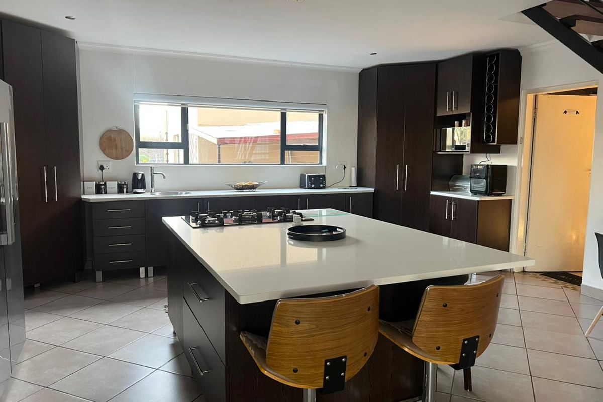 Modern kitchen featuring a large central island with a gas hob, dark wood cabinetry, stone countertops, and tiled flooring.