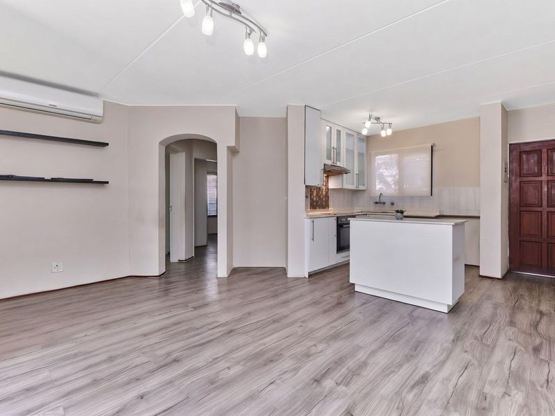 Open-plan living area featuring modern laminate flooring, a split-system air conditioner, and a functional kitchen with built-in cabinetry and a central island.