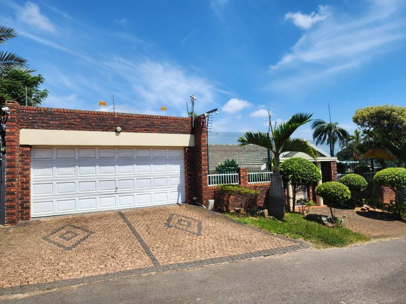 Front exterior view of the property featuring a double garage, paved driveway, and secure perimeter fencing with integrated security systems.