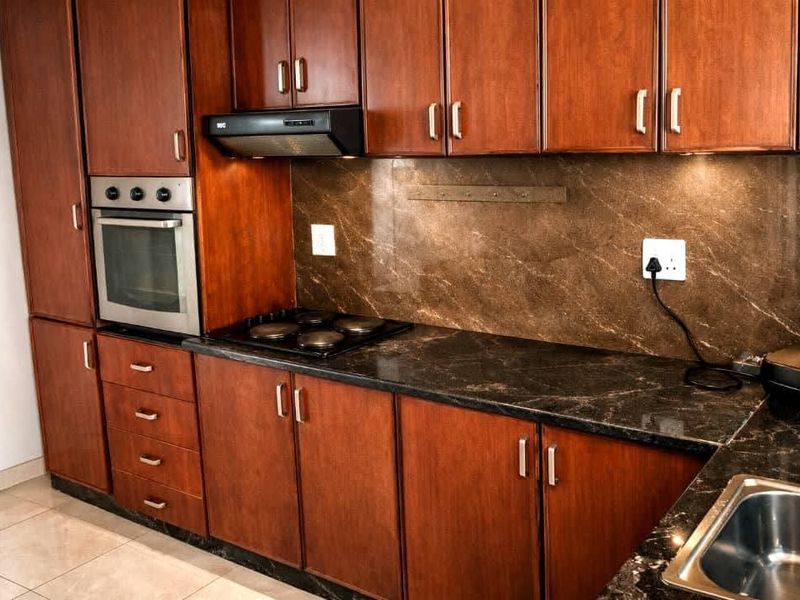 A functional kitchen featuring dark wood cabinetry, stone countertops, a built-in oven, electric hob, and a stainless steel sink with tiled flooring.