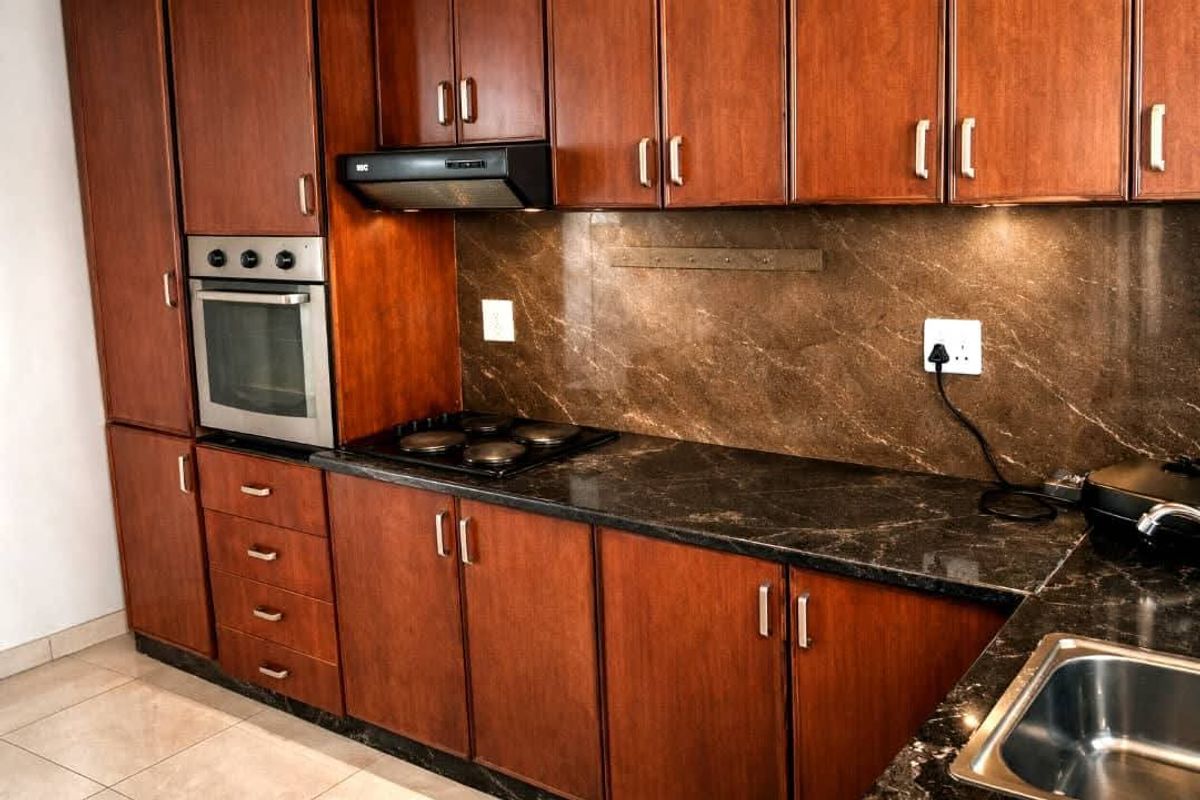 A functional kitchen featuring dark wood cabinetry, stone countertops, a built-in oven, electric hob, and a stainless steel sink with tiled flooring.