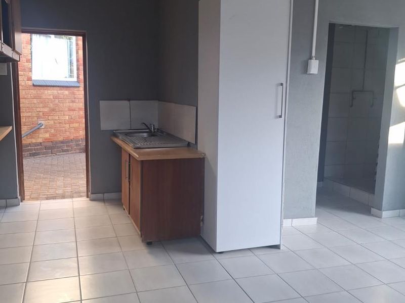 A basic, empty kitchen area featuring tiled flooring, a single sink unit, and built-in cabinetry, with direct access to an exterior courtyard.