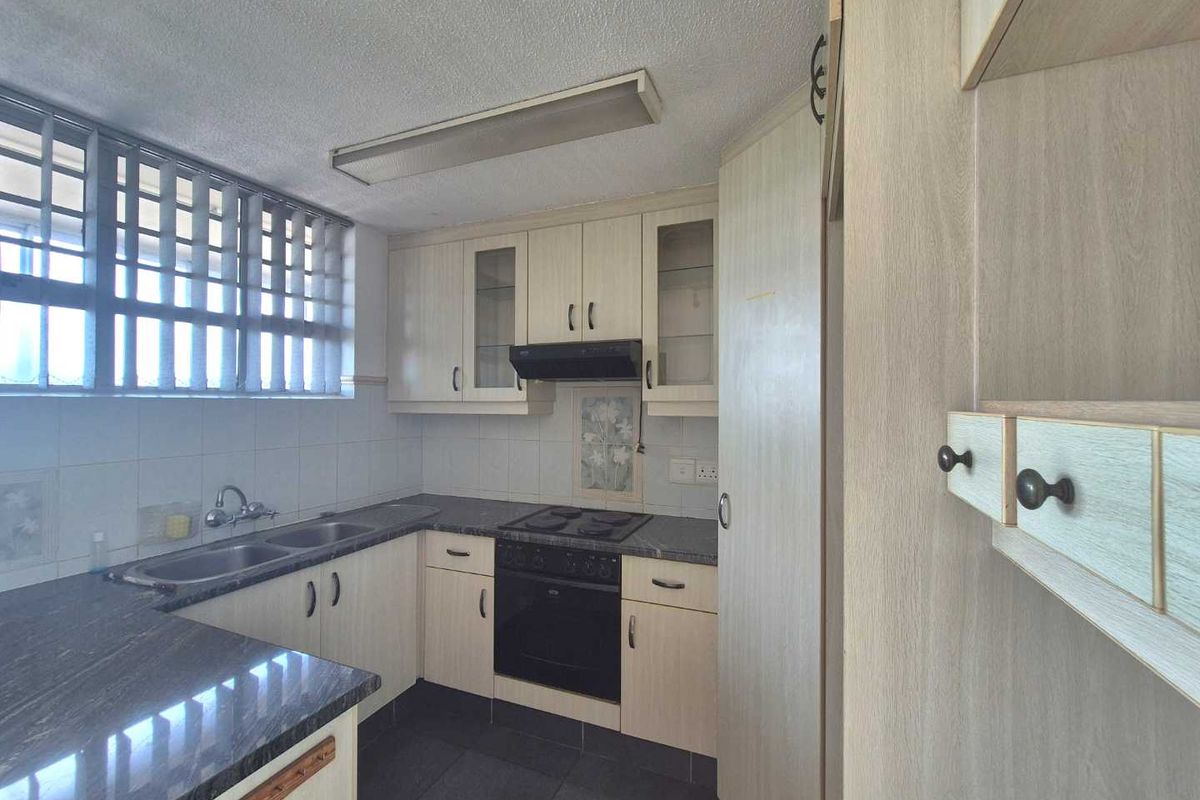 A functional kitchen featuring light-toned cabinetry, dark granite countertops, a built-in oven with hob, and a double-basin sink with tiled splashbacks.