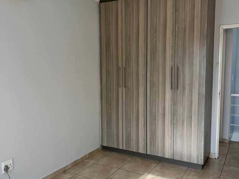 A clean, empty bedroom featuring neutral tiled flooring, a modern wood-finish built-in wardrobe, and a wall-mounted air conditioning unit.