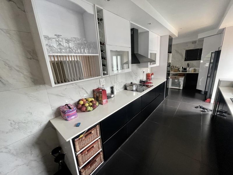 Modern kitchen featuring sleek black and white cabinetry, stone countertops, marble-look wall tiling, and high-quality floor tiles with an integrated hob and extractor.