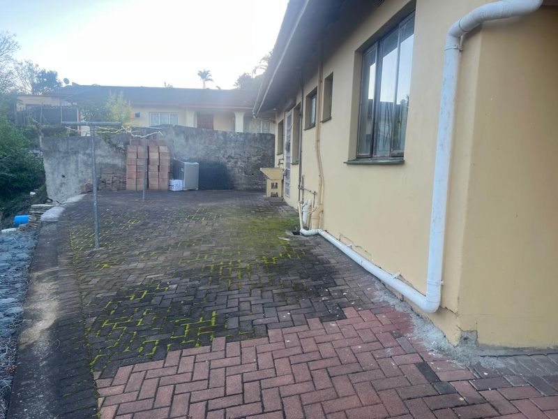 Rear exterior courtyard featuring paved surfaces, an external utility sink, and boundary walling, requiring maintenance and cleaning of the paved area.