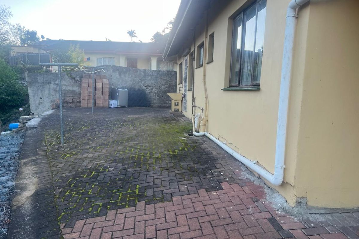 Rear exterior courtyard featuring paved surfaces, an external utility sink, and boundary walling, requiring maintenance and cleaning of the paved area.