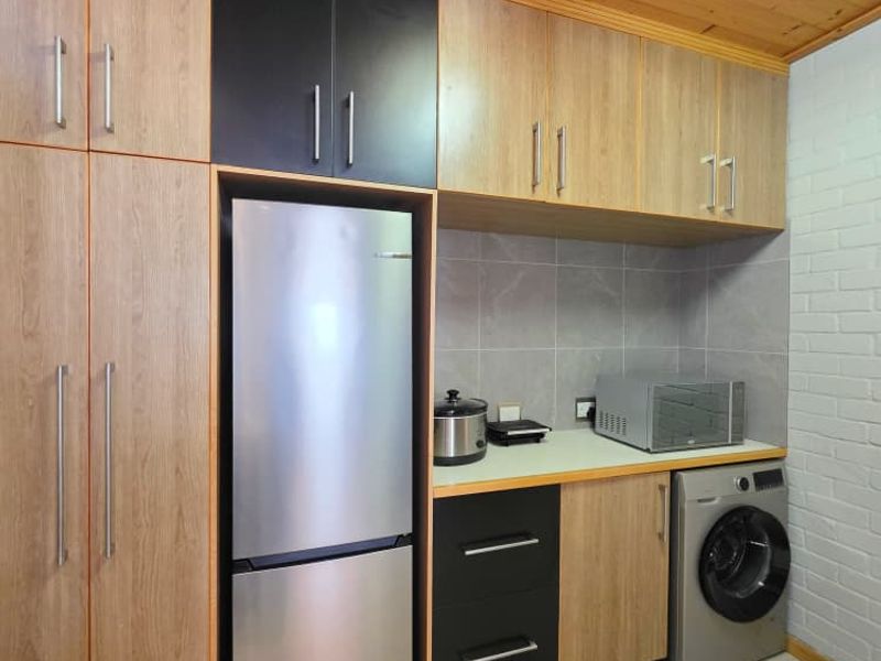 A functional laundry area featuring modern wood-tone and black cabinetry, tiled splashback, and integrated space for laundry appliances under a timber-clad ceiling.