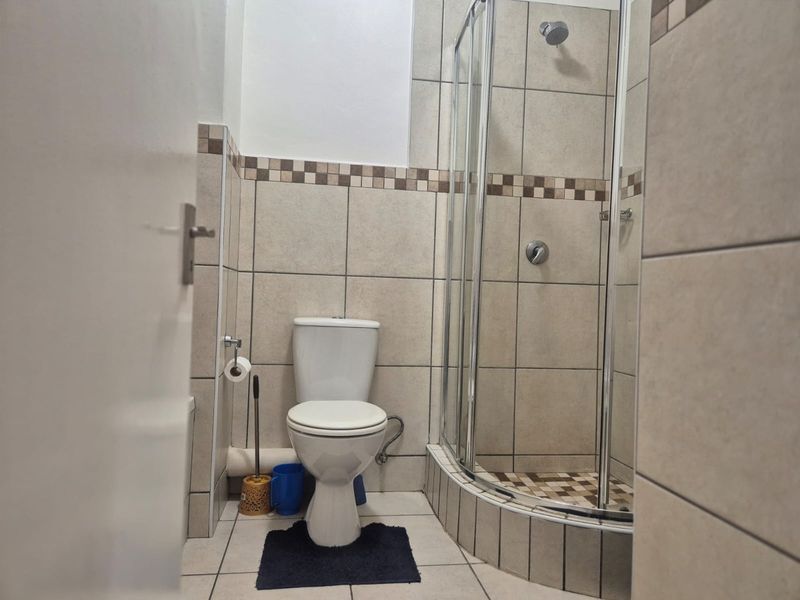 A functional bathroom featuring a corner shower enclosure, toilet, and neutral ceramic tiling throughout.