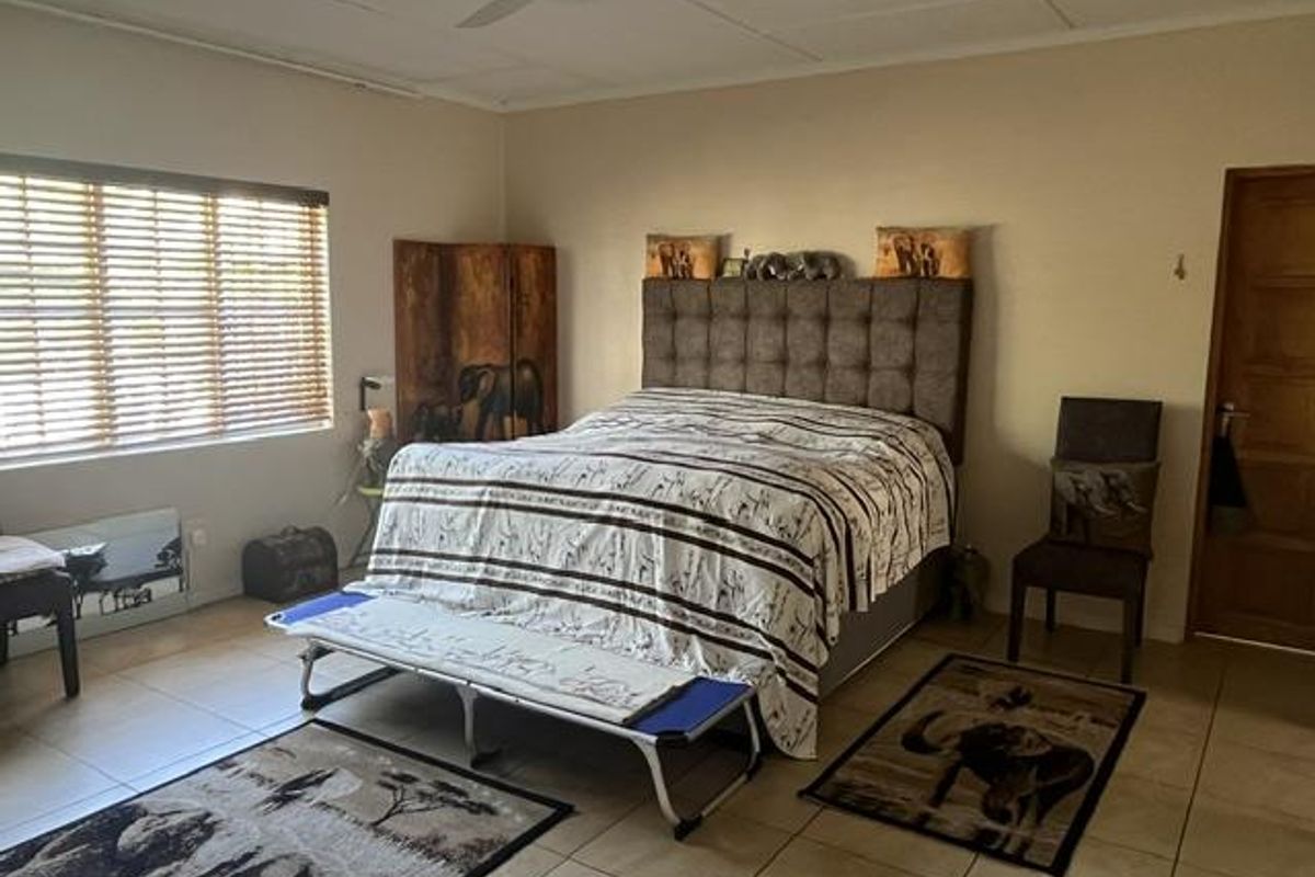 Spacious bedroom featuring tiled flooring, a ceiling fan, and large windows with fitted blinds, offering a functional and comfortable living space.