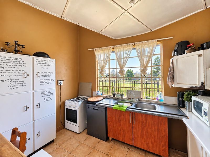 A functional kitchen featuring a double basin sink, tiled flooring, and a large grid window providing natural light and garden views.