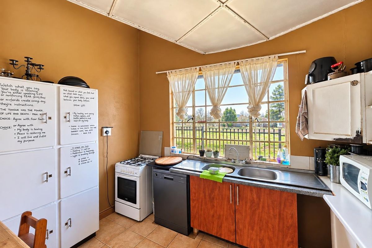 A functional kitchen featuring a double basin sink, tiled flooring, and a large grid window providing natural light and garden views.