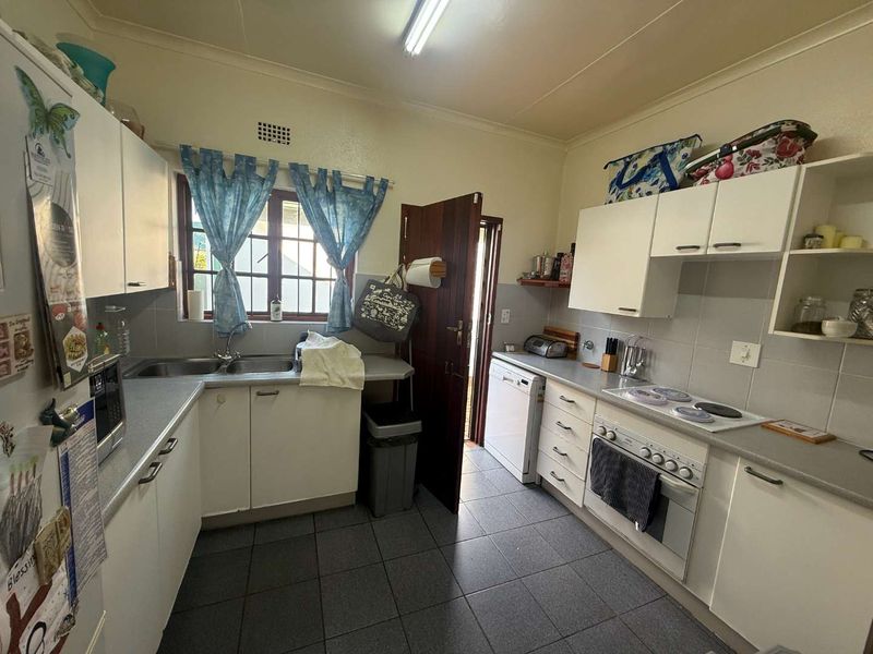 A functional kitchen featuring white cabinetry, tiled splashbacks, a double basin sink, and built-in electric cooking appliances with tiled flooring.