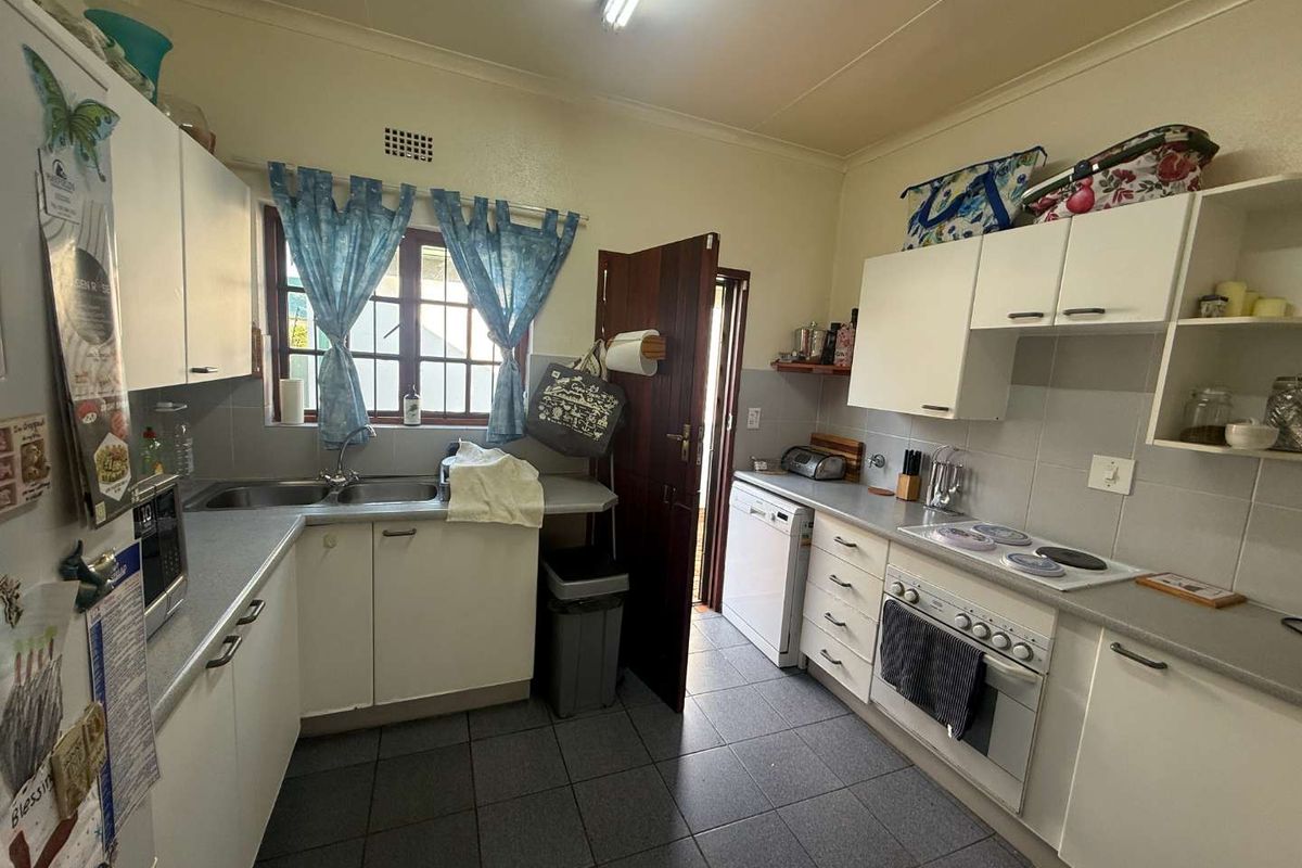 A functional kitchen featuring white cabinetry, tiled splashbacks, a double basin sink, and built-in electric cooking appliances with tiled flooring.