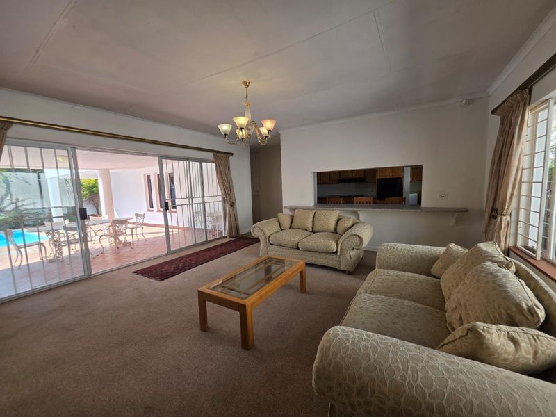 Spacious living room featuring carpet flooring, a breakfast bar opening to the kitchen, and large sliding doors providing access to the patio and pool area.