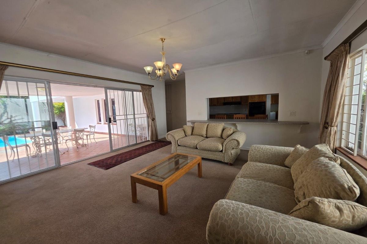 Spacious living room featuring carpet flooring, a breakfast bar opening to the kitchen, and large sliding doors providing access to the patio and pool area.