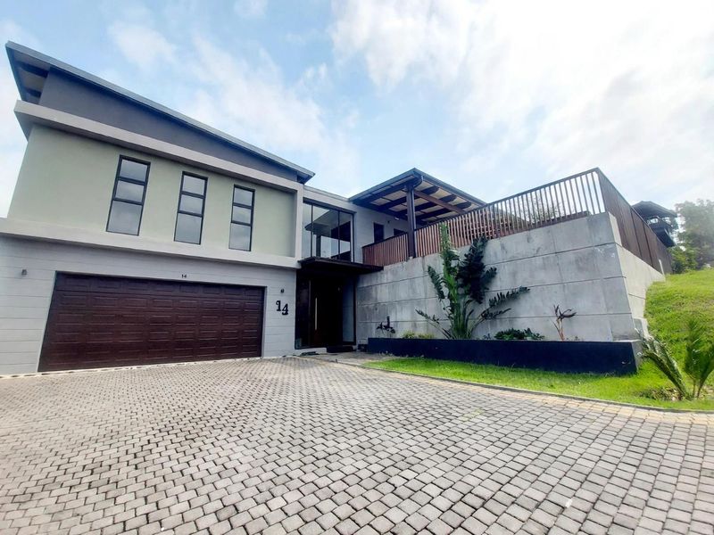 Modern double-storey residence featuring a paved driveway, integrated double garage, and a raised terrace with timber pergola and contemporary architectural finishes.