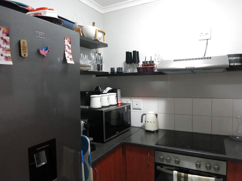 A compact kitchen featuring dark cabinetry, laminate countertops, a built-in oven with electric hob, and a stainless steel extractor fan.
