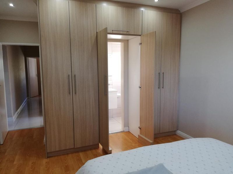 A well-maintained bedroom featuring light wood-finish built-in cupboards, laminate flooring, and direct access to an en-suite bathroom.