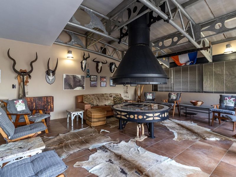 Spacious living area featuring industrial-style exposed steel roof trusses and a prominent central suspended fireplace with tiled flooring throughout.