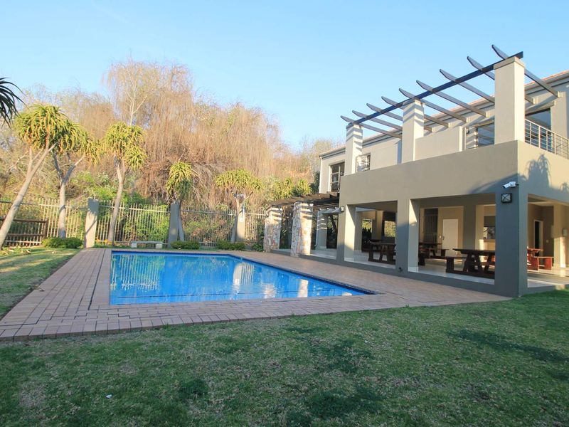 A well-maintained outdoor area featuring a swimming pool with brick coping, a covered patio with a timber pergola, and a landscaped garden.