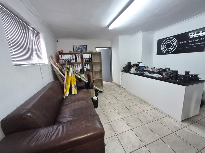 An industrial office space featuring tiled flooring, fluorescent lighting, and a built-in counter, suitable for a professional workspace or studio.