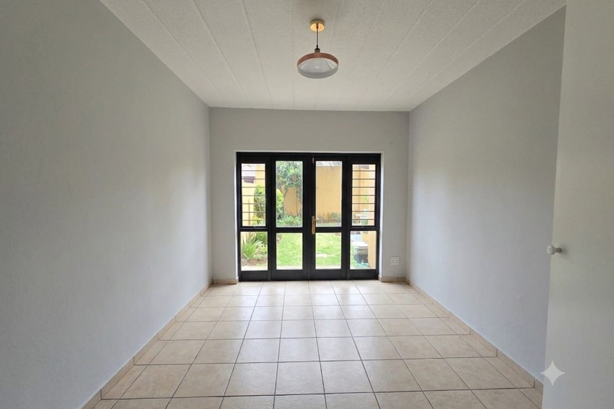 A bright, empty living room featuring neutral tiled flooring and double french doors providing direct access to the rear garden.